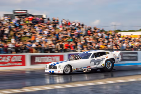 A dragster racing down the strip in front of a packed grandstand
