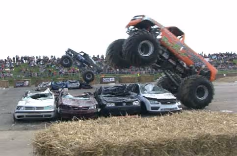 A monster truck rearing up over a row of crushed cars