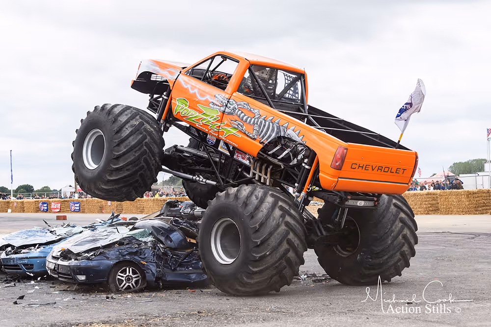 Podzilla, an orange Chevrolet monster truck, on top of crushed cars